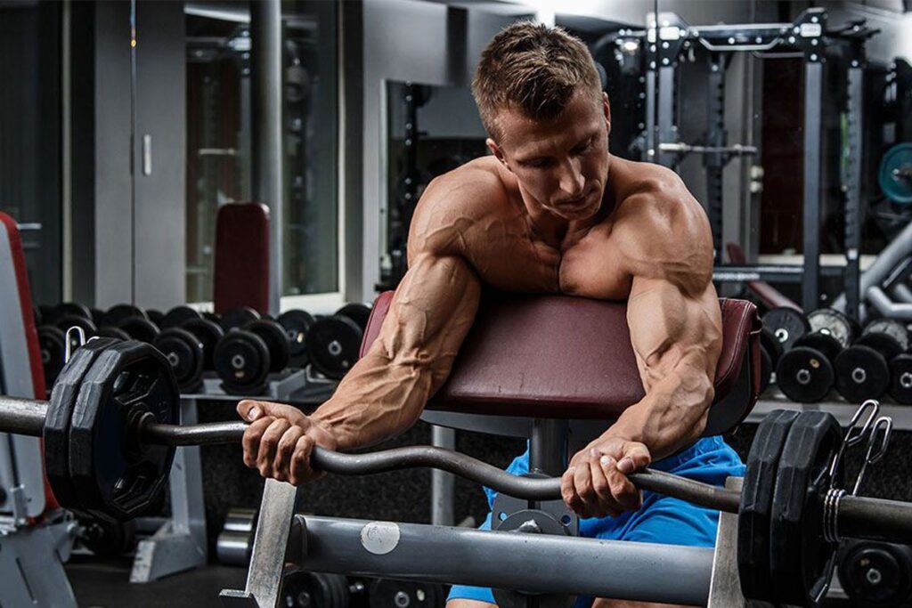 athlete lifting a barbell using the preacher curl bench