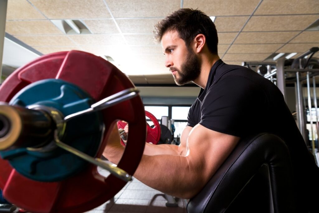 Man Lifting A Barbell Using The Preacher Curl Bench