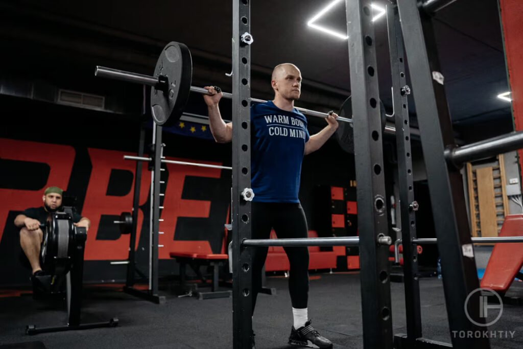 athlete lifts barbell by squat rack